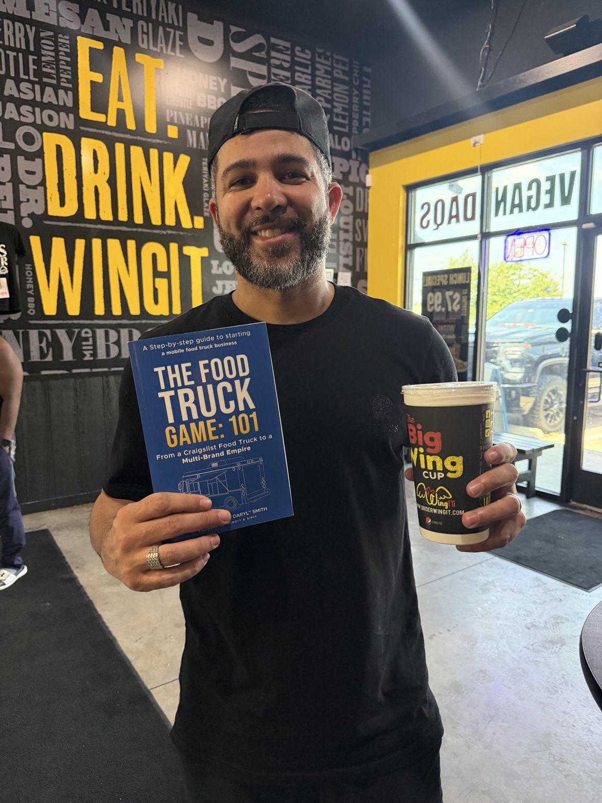 Reader holding The Food Truck Game: 101 and a Big Wing cup inside WingIt