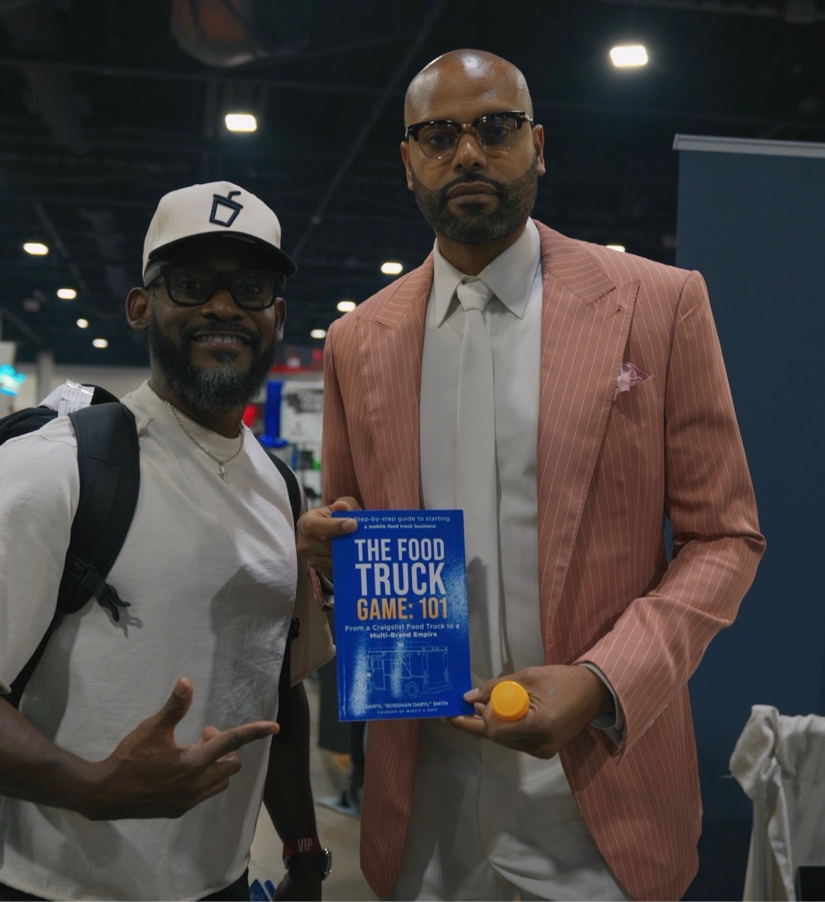 Reader in a pink pinstripe suit holding The Food Truck Game: 101 with Bossman Daryl at an expo
